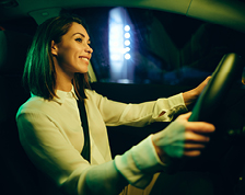 Woman with brown hair smiles while sitting in the driver’s seat with her hands on the wheel. 